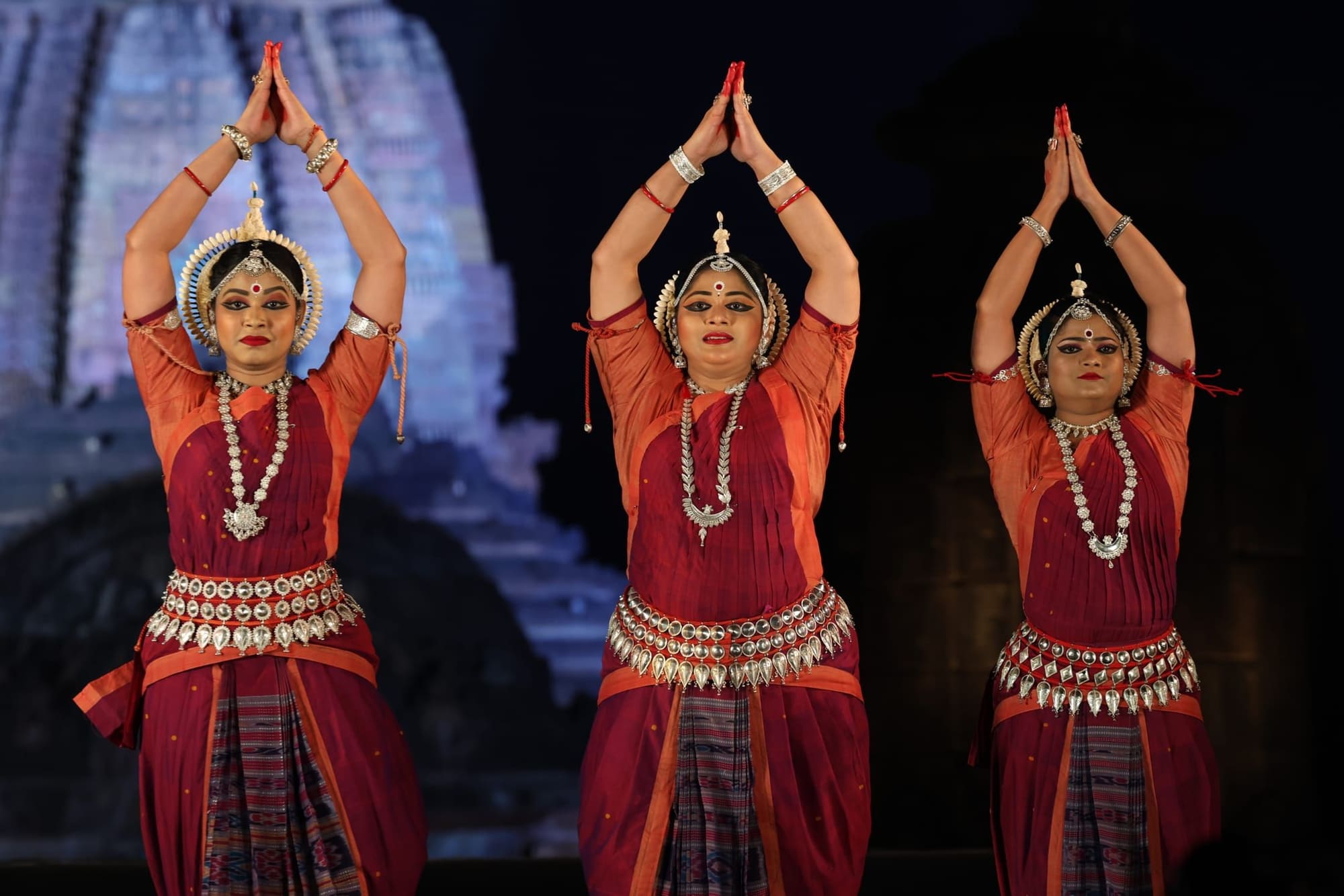 Trio of Odissi dancers with raised namaskar mudra, temple backdrop