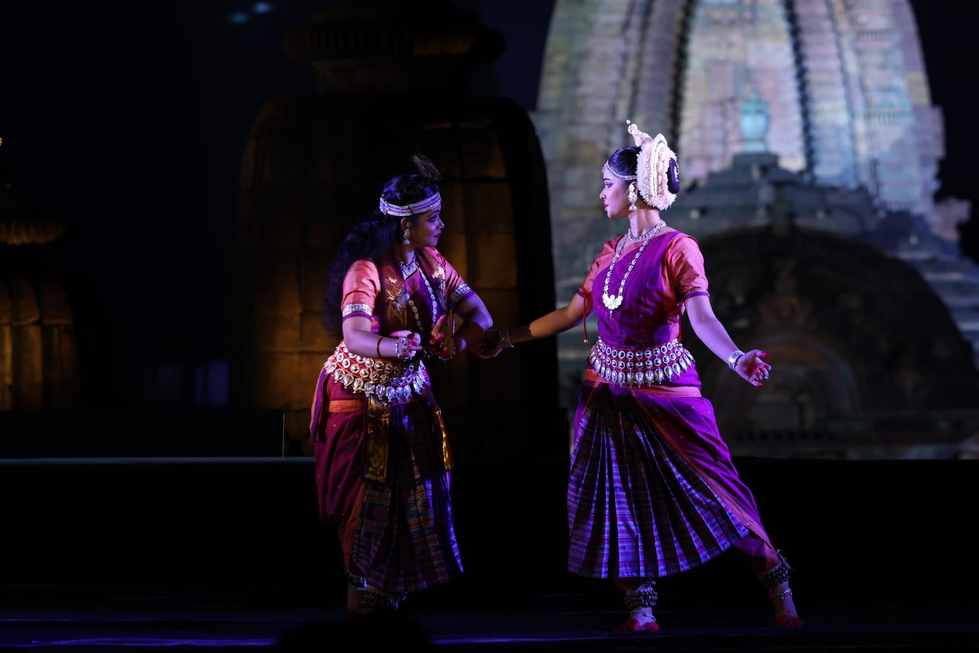 Two Odissi dancers in expressive abhinaya duet, temple backdrop