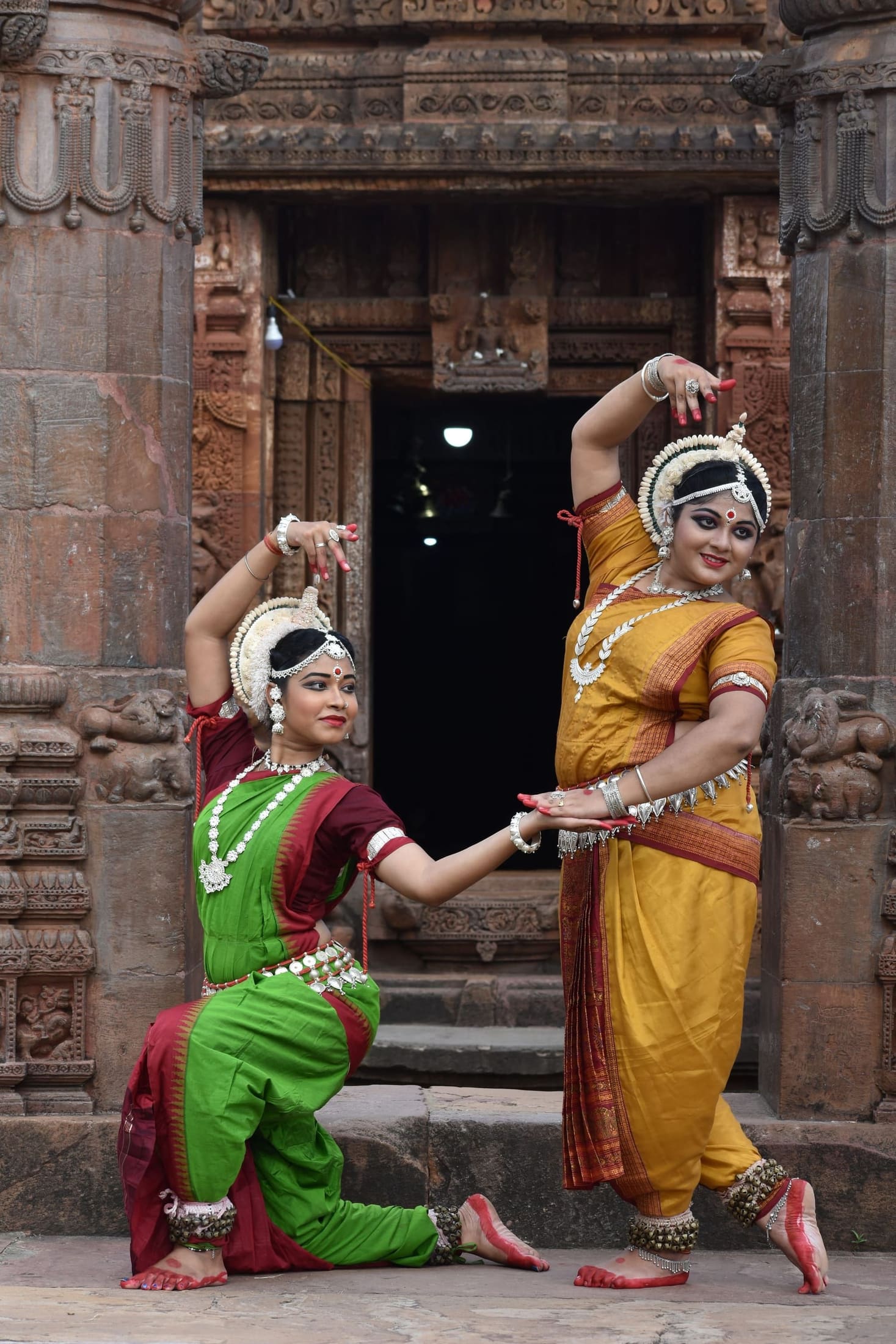 Two Odissi dancers posing at an ancient carved temple doorway