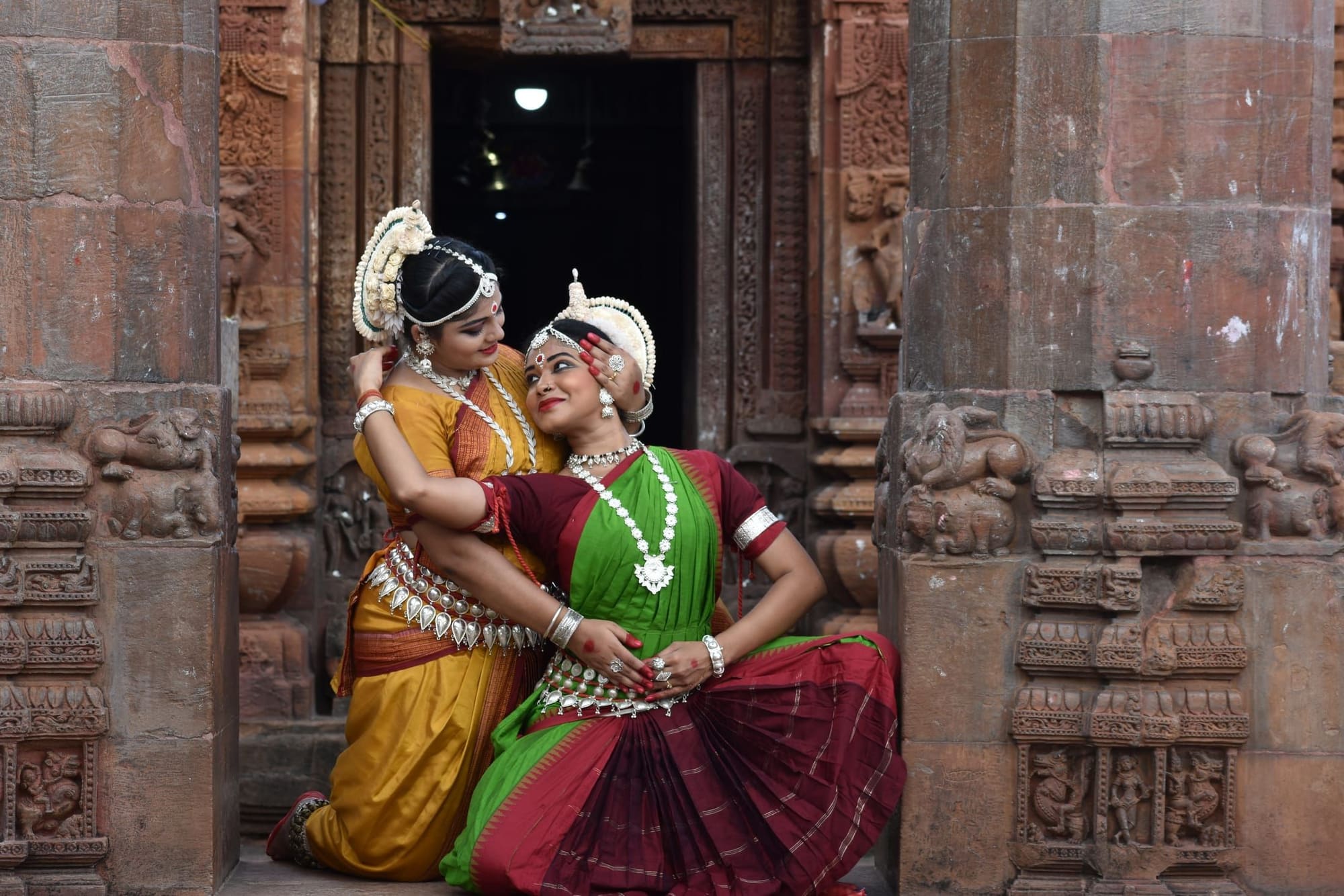 Odissi dancers in a warm embrace at a heritage temple threshold
