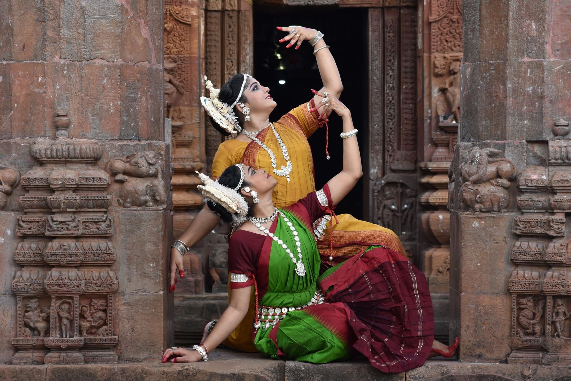 Odissi dancer in green costume seated at ancient temple carvings