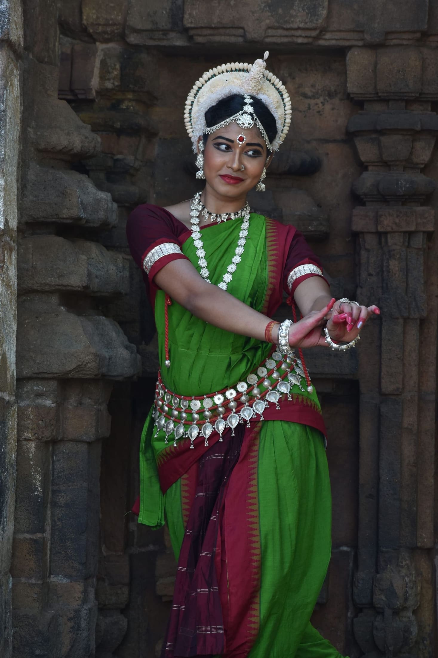 Odissi dancer with raised arm gesture against temple stone
