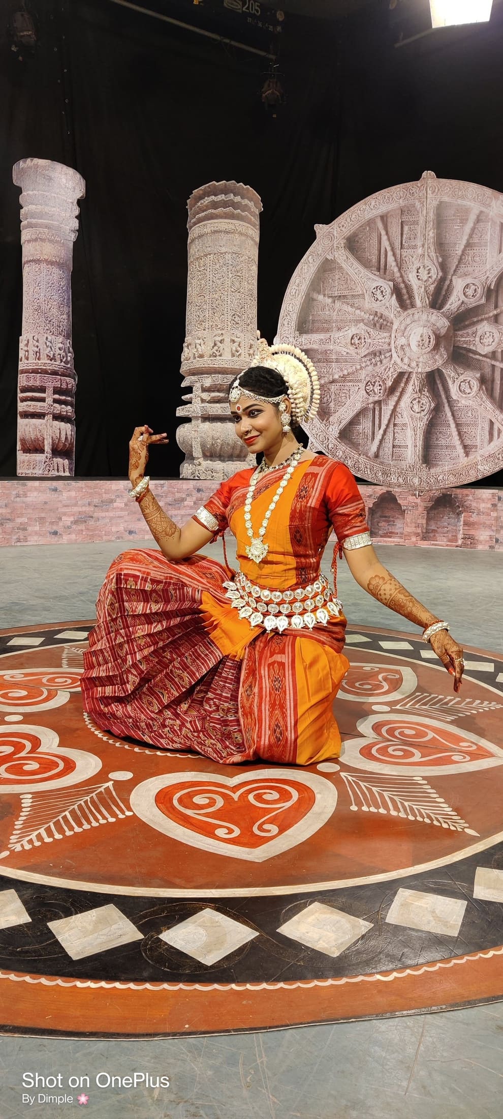 Odissi dancer with henna-adorned hands against a Konark wheel backdrop