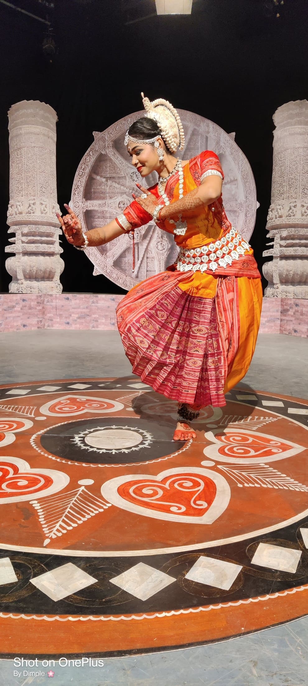 Odissi dancer in dynamic pose against a Konark wheel stage backdrop