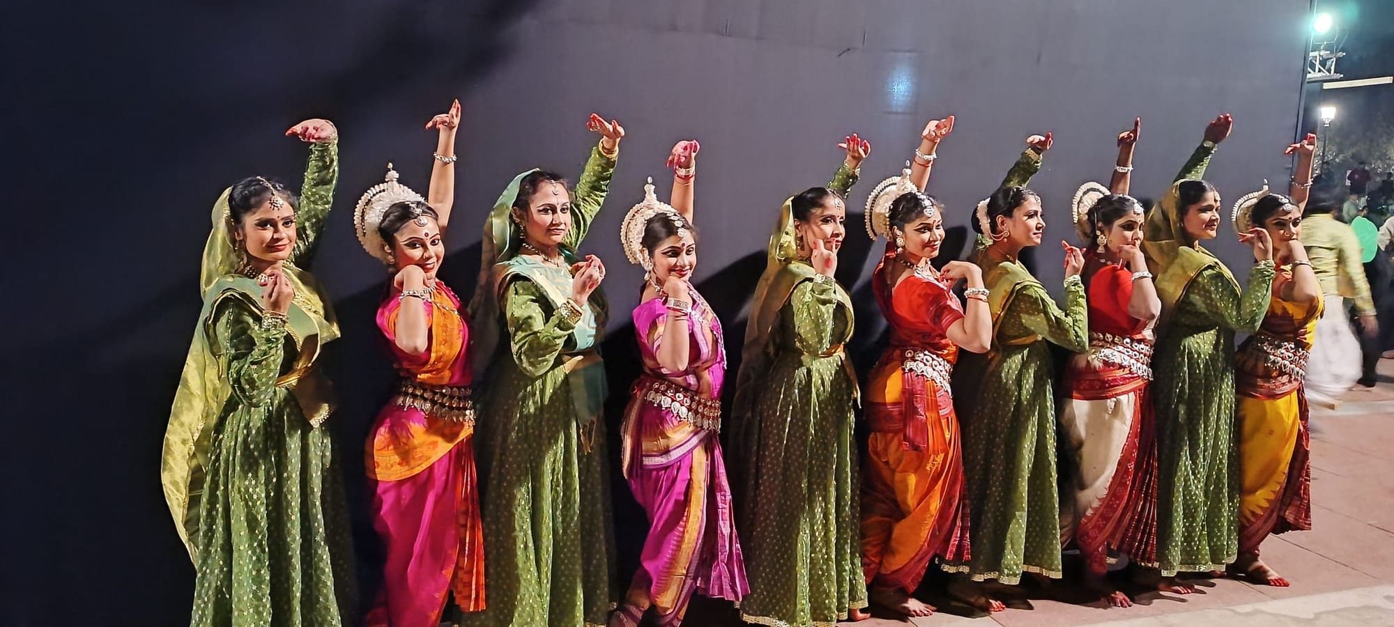 Row of Odissi dancers in matching abhinaya gesture, outdoor evening stage