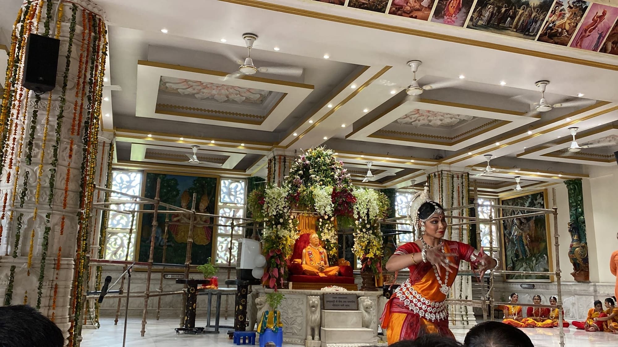 Odissi dancer performing inside a temple hall, students seated nearby