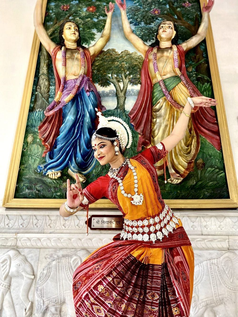 Odissi dancer performing before a painted Krishna-Radha temple mural
