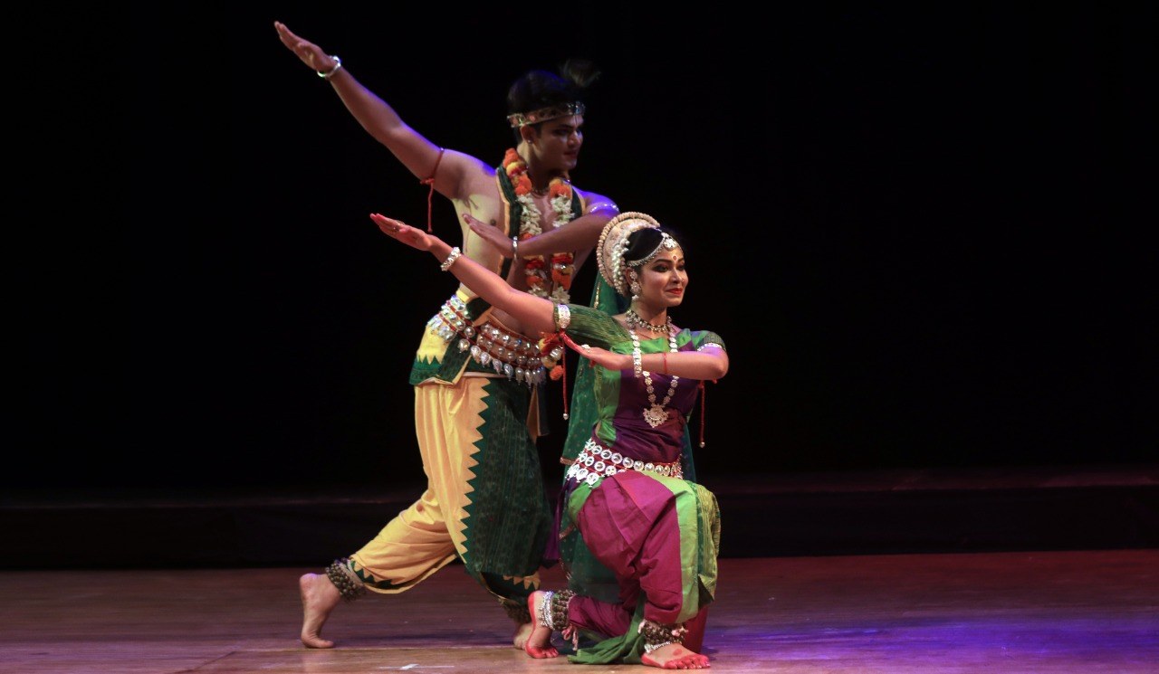 Odissi duet in dynamic diagonal pose under dramatic red stage lighting