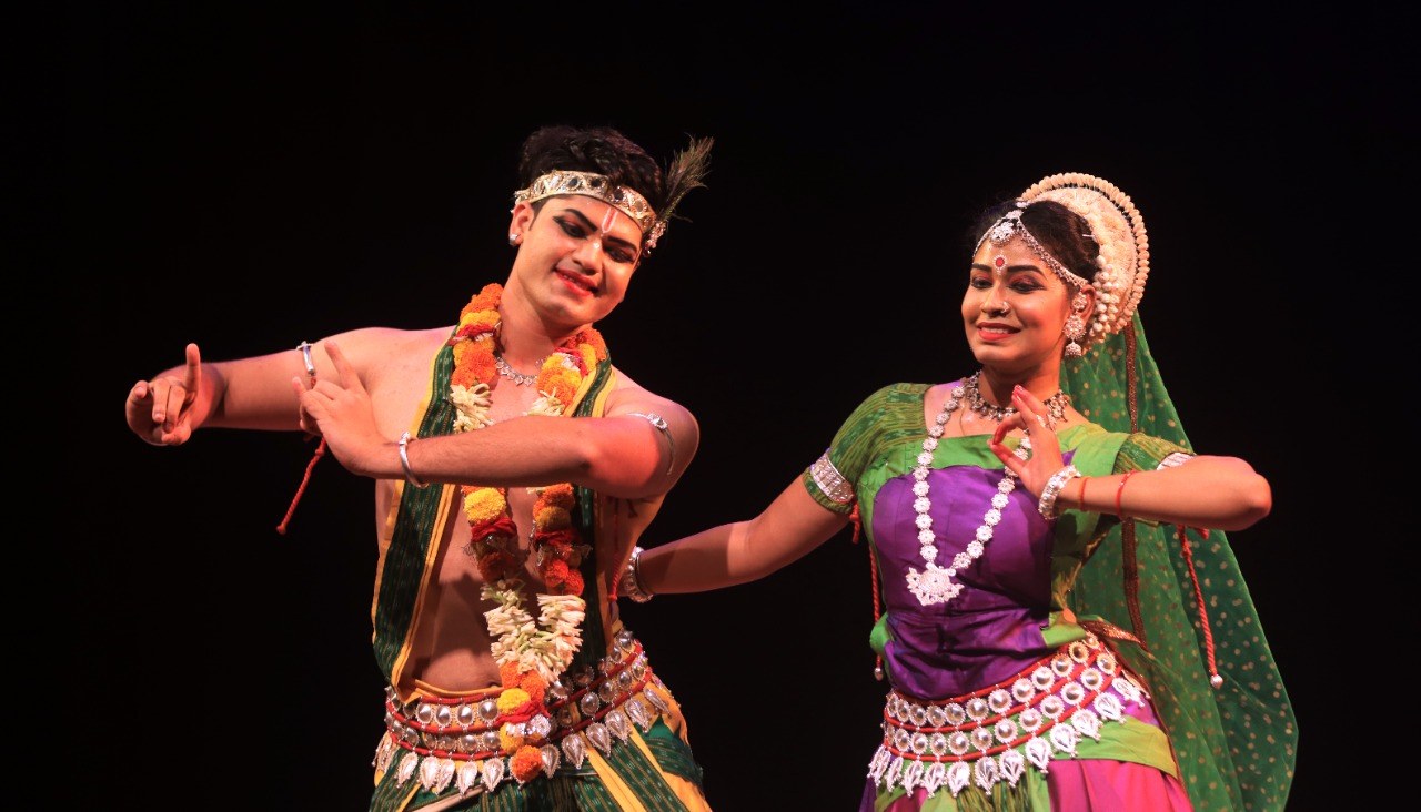 Odissi duet in Radha-Krishna costume, warm smiling expression on stage