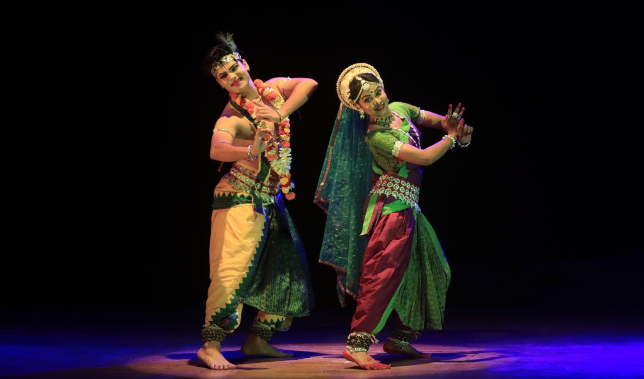 Odissi duet in teal and maroon costume, joyful expression on stage