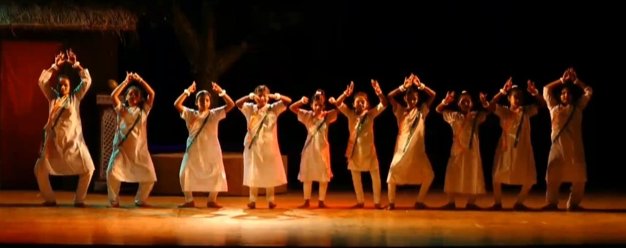 Line of young students in folk costume with hands raised in namaste on stage