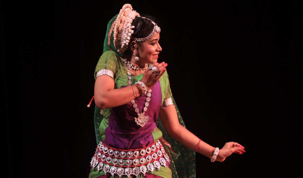Solo Odissi dancer in purple and green costume, side profile on stage